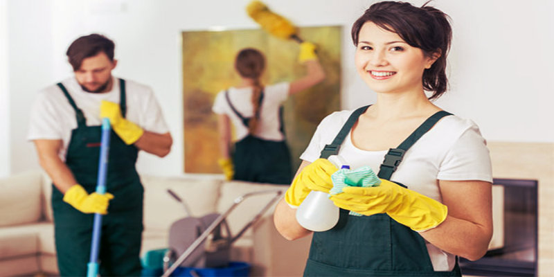 two women and one man in green uniform dusting and mopping in living room