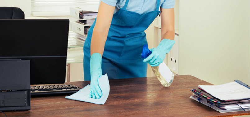 young woman wiping office table and holding spray bottle in hand