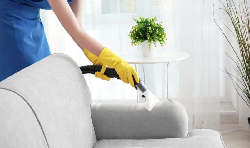 young woman wearing yellow gloves and vacuuming a couch