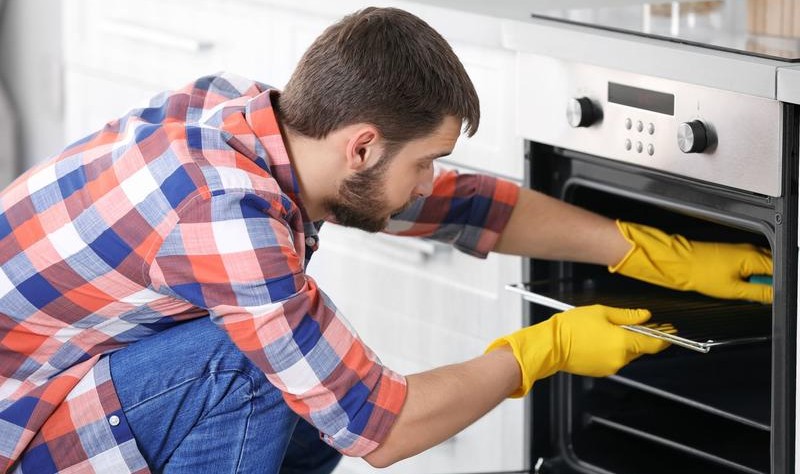 young man with check shirt and yellow gloves fixing an oven