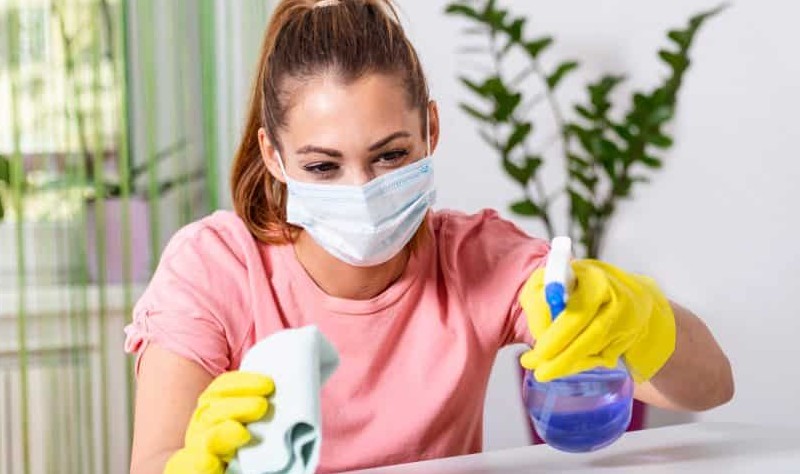 young woman wearing a face mask disinfecting a surface
