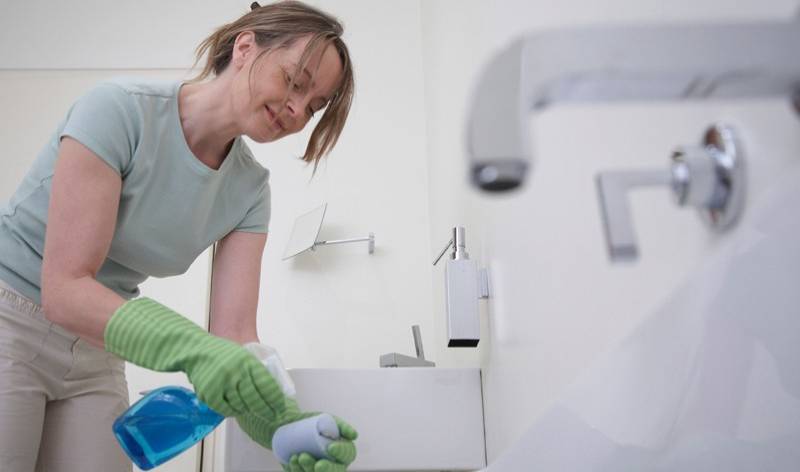 Woman with spray bottle in hand spraying inside a bathroom