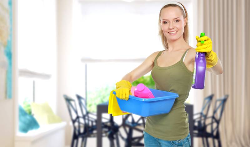 Woman holding blue basket in one hand and a spray bottle in second hand