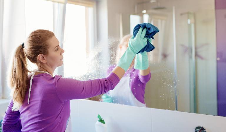 Woman in purple dress washing a mirror inside her bathroom