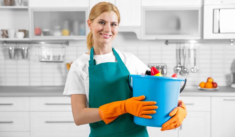 Woman in orange gloves holding a blue basket filled with tools and supplies