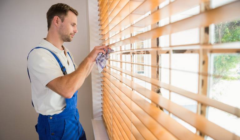 Man in blue white dress holding wooden blind of a window