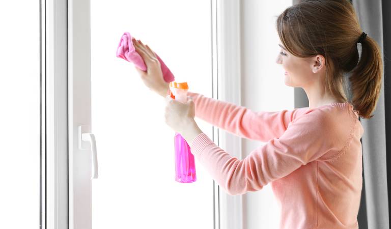Woman in pink dress holding pink bottle and scrubbing window with pink cloth