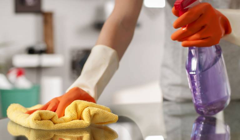 Woman holding a purple bottle in her hand scrubbing a surface with yellow cloth.
