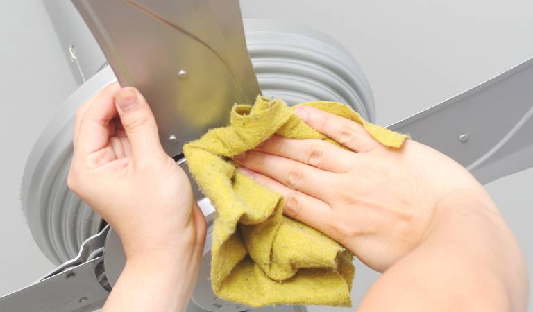 Hand of a man cleaning ceiling fan with a cloth.