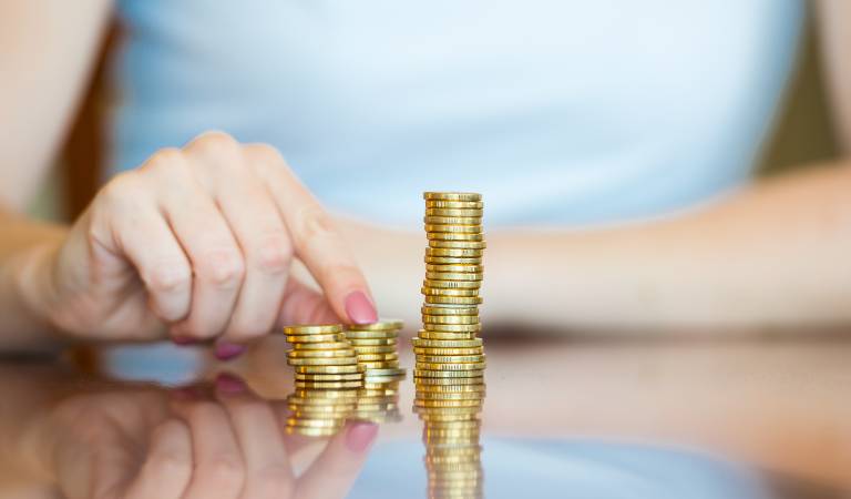 Woman in blue top counting some coins on a table.
