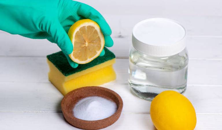 Hand in green glove holding a lemon with baking soda on a table.