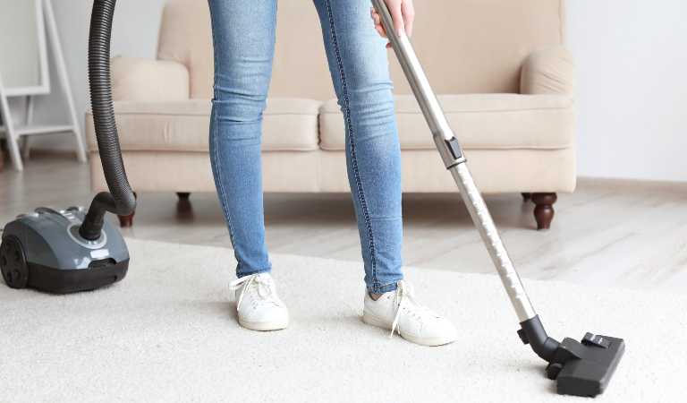 Woman is vacuuming carpet with vacuum cleaner inside a living room