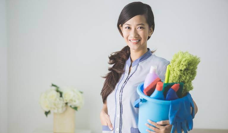 Woman holding a blue basket filled with tools, supplies and bottles.