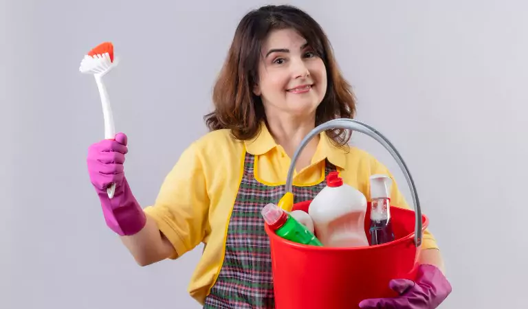 womna with a bucket full of cleaning supplies looking happy