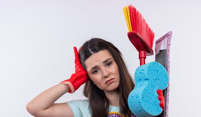 young woman looking worried holding some cleaning supplies