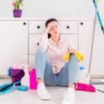 Woman sitting on floor with cleaning tools and put hand on her head