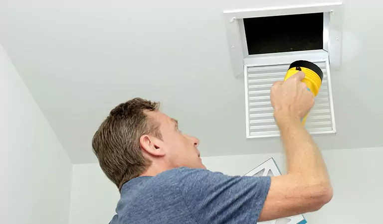 young man inspecting a vent inside of a house
