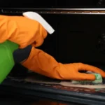 Woman cleaning oven with sponge and detergent closeup