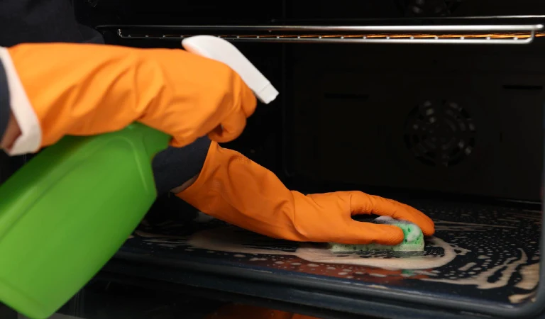 Woman cleaning oven with sponge and detergent closeup