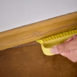 Cleaning a wooden floor baseboard using a yellow brush for optimal hygiene and cleanliness