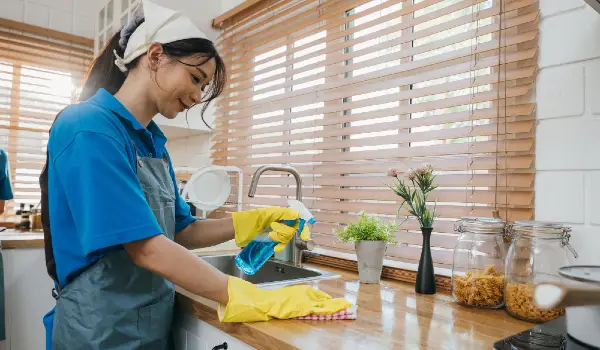 Portrait of smiling woman in uniform cleaning kitchen worktop with spray and cloth housekeeping