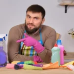 Young handsome bearded man in the kitchen, shows all his cleaning staff - detergents, brushes, sprays. He think he is ready for real cleaning