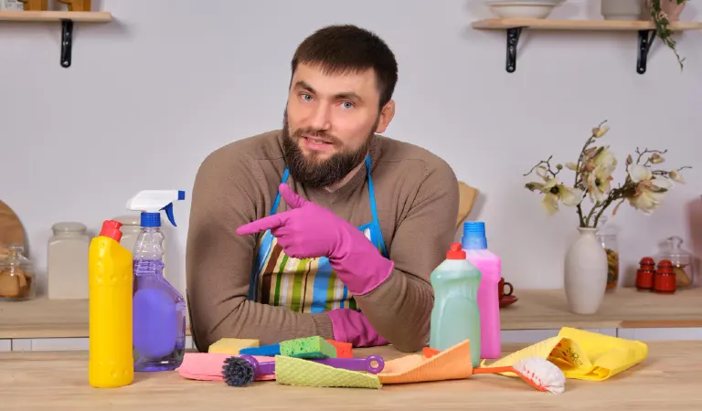 Young handsome bearded man in the kitchen, shows all his cleaning staff - detergents, brushes, sprays. He think he is ready for real cleaning