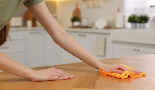 Woman with microfiber cloth cleaning wooden table in kitchen closeup