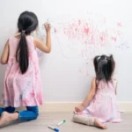 Young sibling kid girl enjoy paint on white wall in living room fun drawing and coloring at home