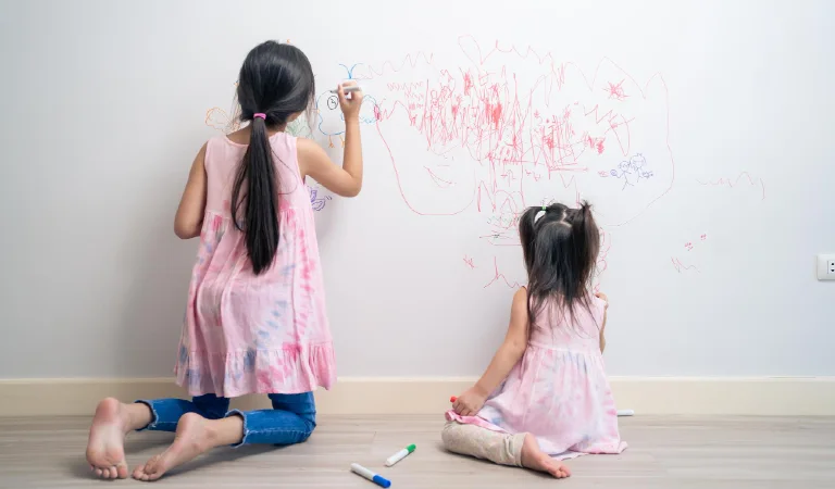 Young sibling kid girl enjoy paint on white wall in living room fun drawing and coloring at home